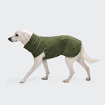 Ein weißer Hund läuft, bekleidet mit dem Body Warmer AKTIV Khaki – einem khakifarbenen Fleece-Pullover, der seinen Körper und Hals bedeckt. Der Hintergrund ist einfarbig hellgrau.