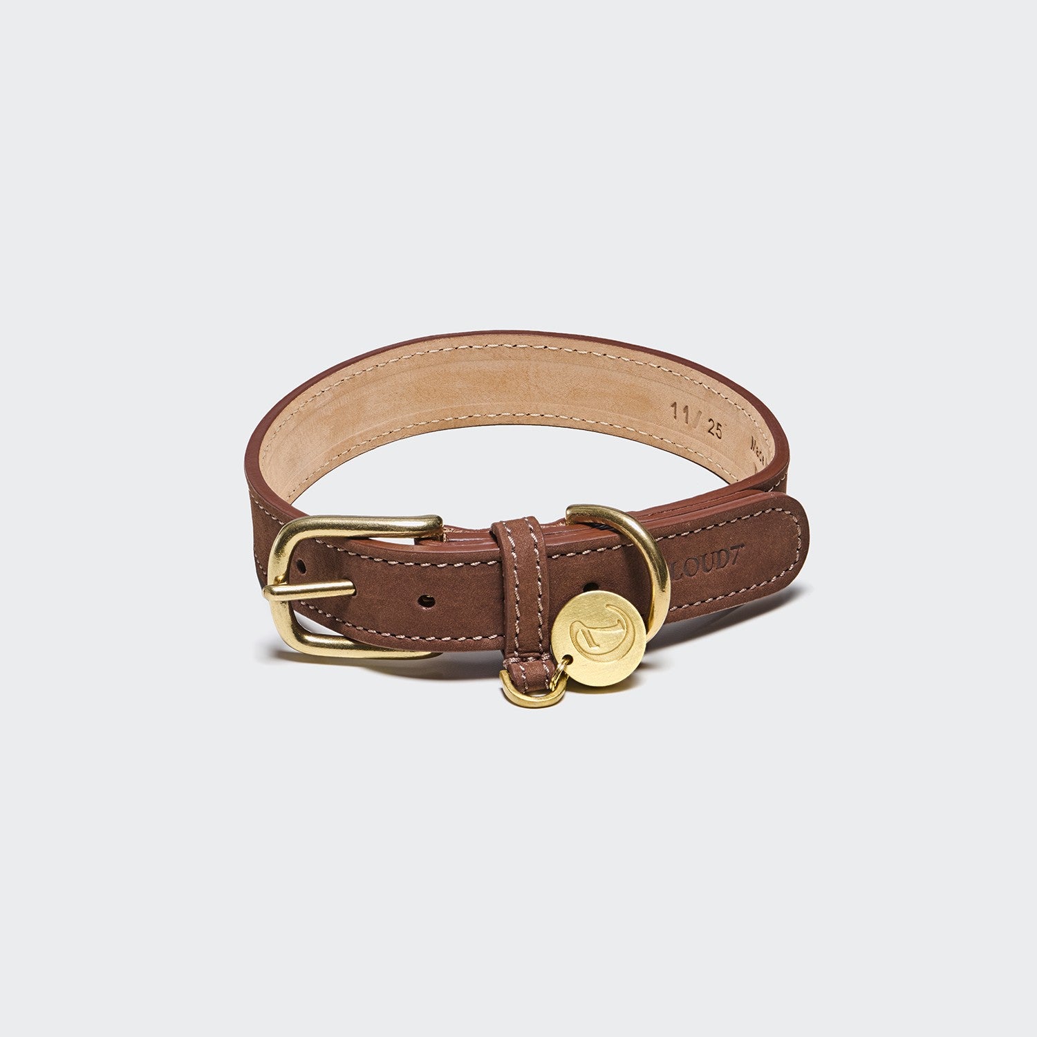Hundehalsband Tiergarten Mocca: Braunes Hundehalsband aus Nubukleder mit goldener Schnalle, D-Ring und einer runden goldenen Plakette, abgebildet auf hellgrauem Hintergrund. Dieses Halsband besticht durch sichtbare Nähte und einen geprägten Markennamen an der Seite und vereint klassischen Stil mit robuster Verarbeitung für Ihren Hund.