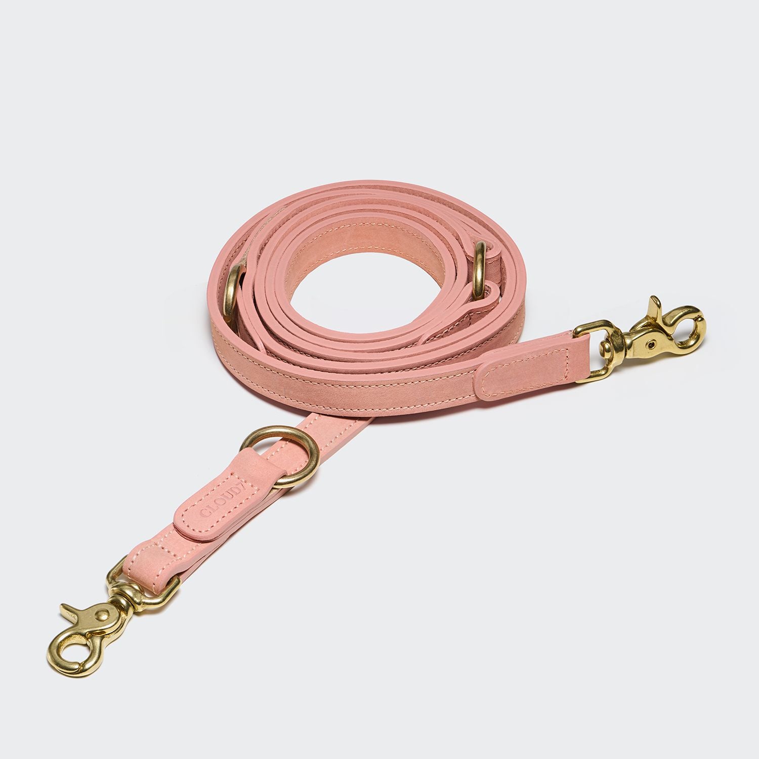 Eine Hundeleine „Tiergarten Peach“, längenverstellbar und aus pinkfarbenem Nubukleder mit goldfarbenen Metallverschlüssen und -ringen, ordentlich aufgerollt auf einem schlichten, hellen Hintergrund.