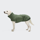Ein gelber Labrador Retriever, der den „Derby 2.0“-Hundepullover in Khaki aus recyceltem Fleece trägt, steht auf einem hellgrauen Hintergrund und blickt nach links.