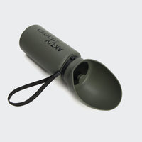 CLOUD7_ Die Hundetrinkflasche AKTIV Dark Olive ist eine grüne, faltbare Trinkflasche für Haustiere mit angebrachter Schale und schwarzem Band, die mit AKTYLZMOD beschriftet ist und auf einem hellgrauen Hintergrund abgebildet ist - ideal für Outdoor-Abenteuer mit Ihren pelzigen Freunden.